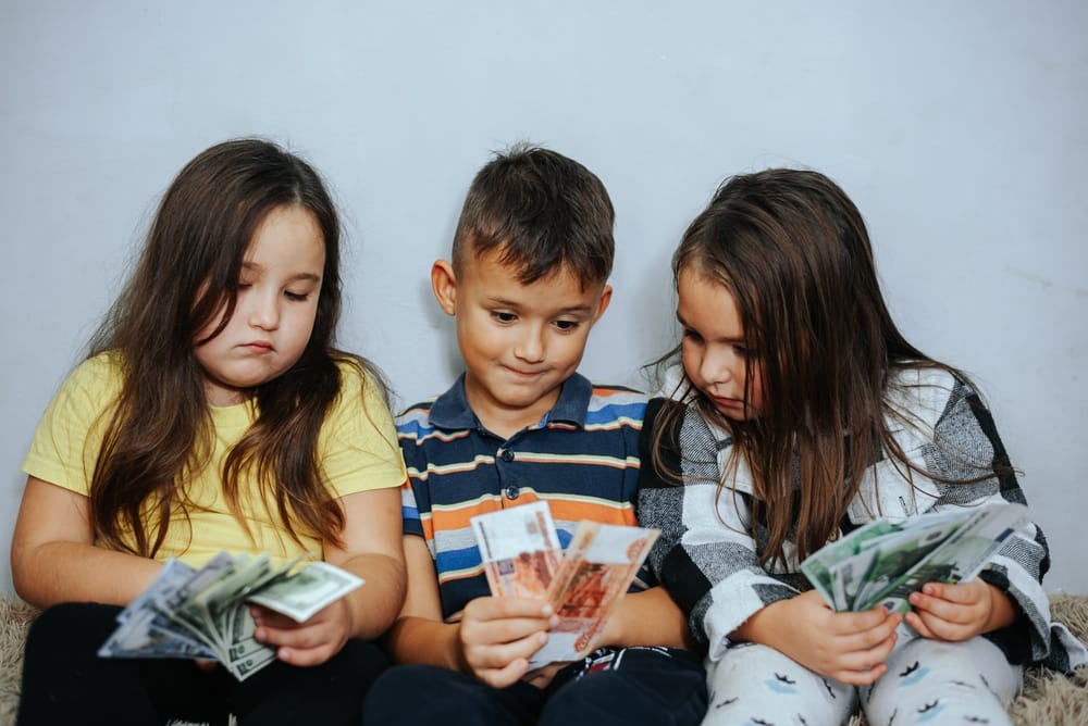 Three children counting coins – planning for the cost of raising a family Three children counting coins on a table, representing the cost of raising children and family financial planning in the UK.