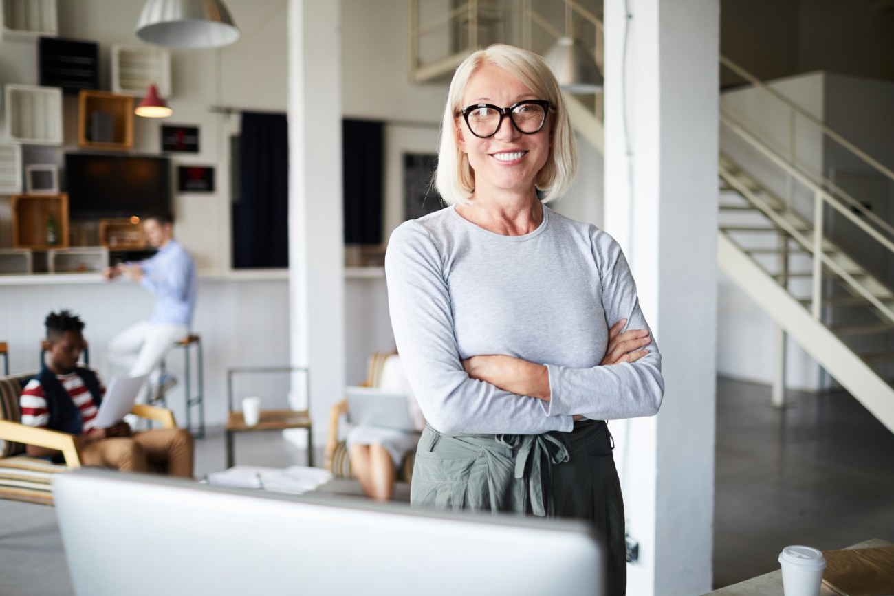 Blond businesswoman Smiling blond woman with crossed arms looking at you by her workplace