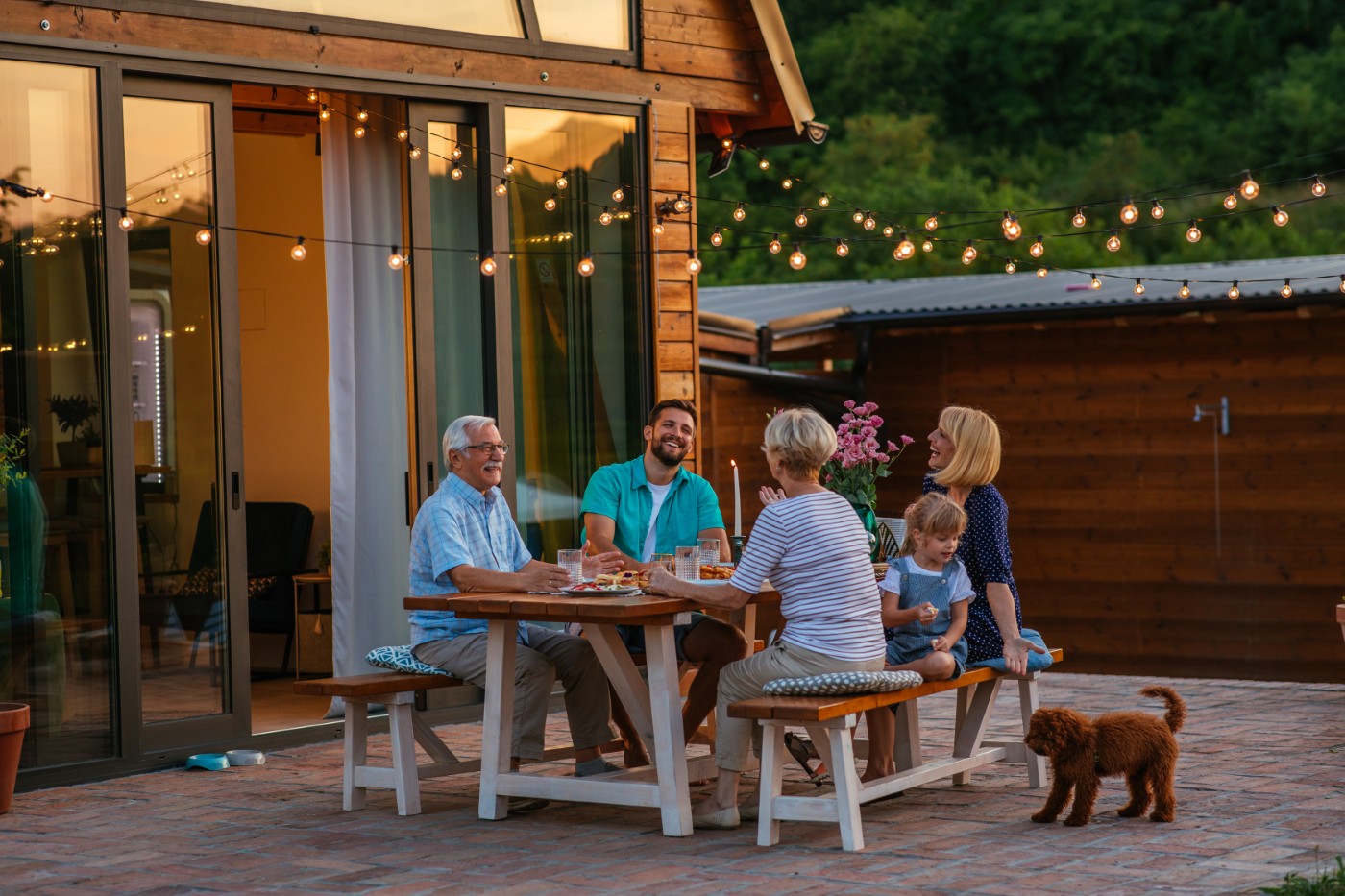 Family dinner around dining table in the garden Happy family eating together outdoors. Smiling generation family sitting at dining table during dinner. Happy cheerful family enjoying meal together in garden.