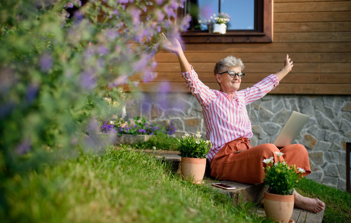 Happy senior woman with laptop working outdoors in garden, home office concept. A happy senior woman with laptop working outdoors in garden, home office concept.